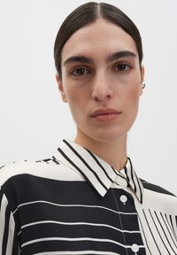 Schwarz-weiß gestreifte Bluse mit Kragen und Knopfleiste. Glatter Stoff mit variierenden Streifenbreiten und lockerem Schnitt.