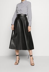 Mustat keinonahka A-linjan hame korkea vyötärö, yhdistettynä raidalliseen nappipaitaan. Ominaisuuksiin kuuluu pitkät hihat ja nilkkakorkokenkä.