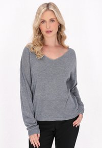 Pulover gri, cu mânecă lungă și decolteu în V, textură moale, croială liberă și mansete cu nervuri, purtat cu pantaloni negri.