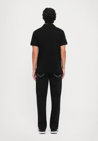 Black polo shirt with a collar, short sleeves, and textured shoulder accents, paired with loose black pants and white athletic shoes.