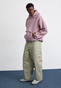 Lila hoodie med orange detaljer och snörning, tillsammans med lösa olivgröna cargobyxor. Texturerad tyg, avslappnad passform och framfickor.