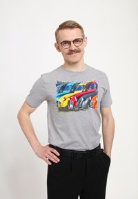 Grå bomulds t-shirt med et farverigt grafisk design af vintage biler i blå, gul, rød og orange. Mændenes bukser er sorte.