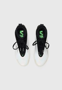 Paire de baskets blanches et noires avec des lacets noirs et des inscriptions vertes à l’intérieur, vues de dessus sur un fond uni.