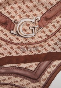 Écharpe en soie marron et beige avec un motif géométrique, la lettre "G" et le mot "GUESS" dans une police décorative.