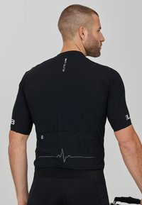 Schwarzes Radtrikot mit kurzen Ärmeln, ausgestattet mit einer Rückentasche und einem Grafikdesign mit Herzschlaglinie. Hergestellt aus leichtem, feuchtigkeitsableitendem Material.