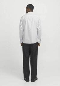 Striped, button-up shirt in light blue and white with long sleeves, worn with dark trousers. The shirt has a rounded hem and a standard collar.