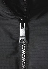 Chaqueta negra con cremallera, presenta un tejido con textura y un patrón de cuadrícula. El tirador de la cremallera es plateado con el nombre de la marca "WEEKDAY" en relieve.