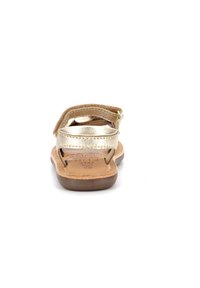 Sandales en métal doré avec une finition texturée, semelle intérieure en cuir marron, bride de cheville adjustable et semelle plate. Design simple pour un enfilage facile.