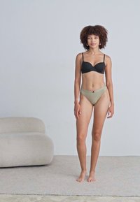 Soutien-gorge noir à fines bretelles associé à un bas de bikini vert olive, avec une taille surpiquée et un design minimaliste, sur un mannequin.