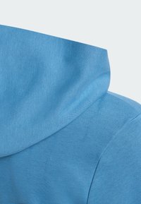 Lyseblå hættejakke med et blødt, tekstureret stof og hætte. Designet har en glat overflade og diskrete syninger.