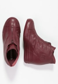 Stivali alla caviglia in pelle bordeaux con finitura liscia, chiusura a zip e dettaglio del logo circolare sul lato. Silhouette elegante e contemporanea.
