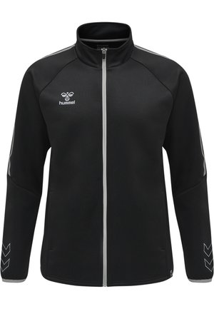 Chaqueta negra con cremallera y cuello alto, con acentos plateados y patrones en forma de chevrón en las mangas. Fabricada con un tejido liso y ligero.