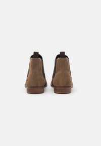 Bottines en suède marron avec des panneaux élastiques sur les côtés et des semelles en caoutchouc marron, dotées d'une texture lisse et d'un design de bout rond.