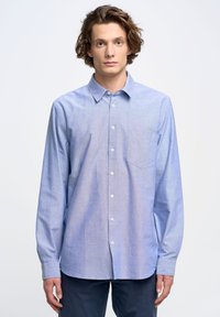 Camisa azul claro de botones con mangas largas, un bolsillo en el pecho y un dobladillo curvado. Hecha de una tela texturizada, con un patrón sutil.