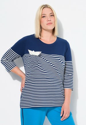 T-shirt rayé bleu marine et blanc à manches 3/4, avec un motif de bateau en papier et une texture de tissu lisse. Assorti avec un pantalon bleu.