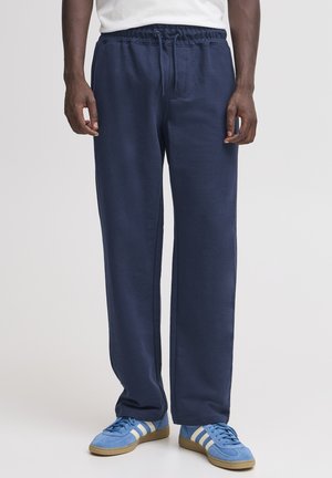Pantaloni della tuta blu navy, realizzati in morbido cotone, con vita elastica e coulisse, vestibilità comoda e tasche laterali. Abbinati a sneakers azzurro chiaro.