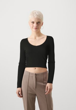Black long-sleeve crop top with a scoop neckline, made from ribbed fabric. Worn with beige high-waisted trousers featuring a front seam detail.