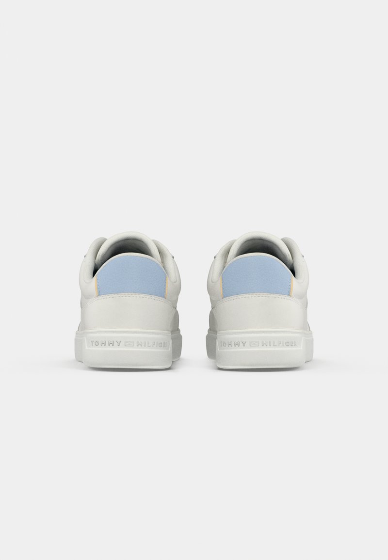 Weiße Low-Top-Sneaker mit hellblauen Fersenpatches, Markenname "Tommy Hilfiger" in die hinteren Sohlen eingeprägt, vor einem einfarbigen Hintergrund.