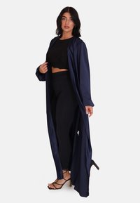 Lång marinblå satinrock med flödande design, långa ärmar och en djup slits. Matchad med en svart crop top och svarta åtsittande byxor. Svarta klackskor med remmar.