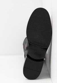 Botín negro hasta el tobillo con un upper de cuero texturizado, tacón negro liso y suela de goma. Presenta un zipper lateral y acentos de hardware dorado.