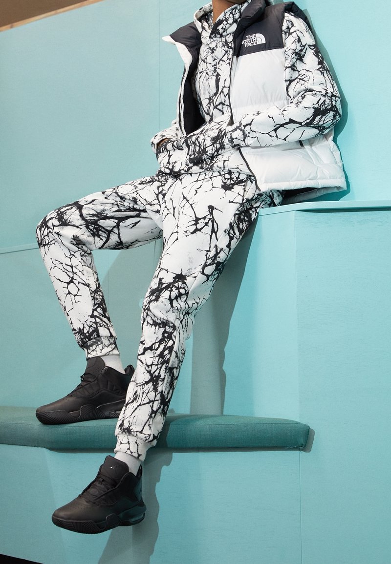 Valkoinen toppaliivi mustilla yksityiskohdilla musta-valkoisen abstraktin kuosin asun päällä. Mustat urheilu kengät viimeistelevät kokonaisuuden.