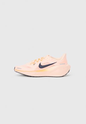 Zapatilla de running Nike de color rosa claro con logo de swoosh negro, parte superior de malla y suela gruesa y acolchada, mostrada de lado sobre un fondo liso.