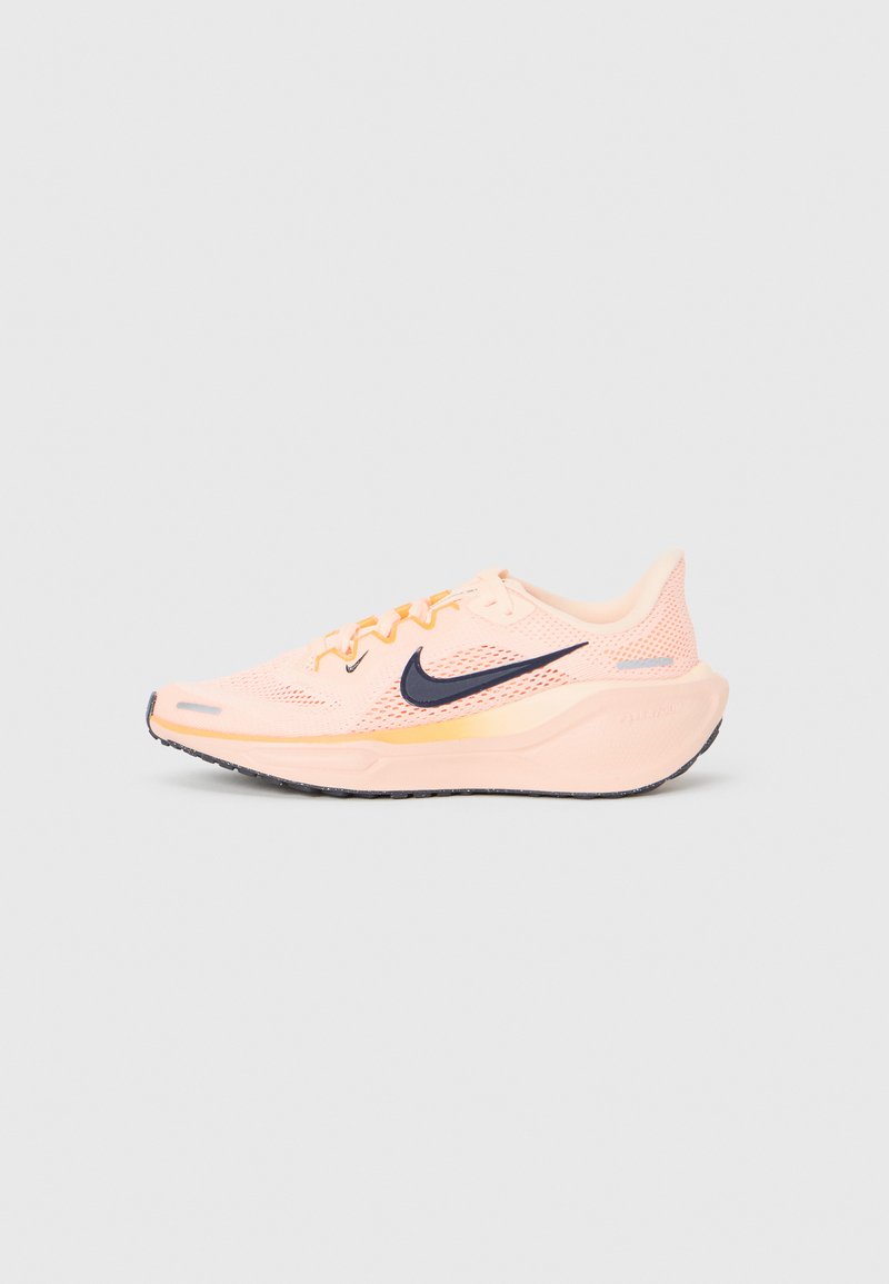 Baskets de course Nike rose clair avec logo swoosh noir, tige en maille et semelle épaisse et rembourrée, présentées de côté sur un fond uni.