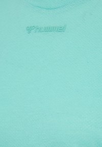 Mint green textured fabric with raised Hummel logo near the top center, featuring a subtle honeycomb pattern.