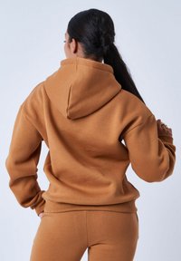 Bruine hoodie gemaakt van zacht, fleeceachtig materiaal. Heeft een capuchon, geribde manchetten en een relaxte pasvorm, gecombineerd met bijpassende joggingbroek.