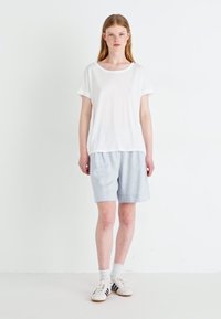 T-shirt blanc à manches courtes et short gris clair. Le T-shirt a un col rond ; le short est ample et fabriqué en tissu doux. Baskets blanches.