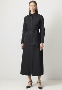 Zwart langarm shirtjurk met een puntkraag, sluiting met knopen aan de voorkant, cinched taille met een strik en een rechte, enkel-lange siloeët.