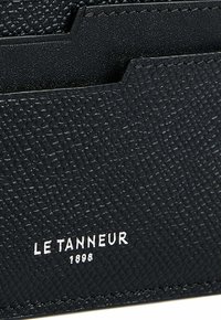 Billetera de cuero negro con una superficie texturizada, que cuenta con ranuras para tarjetas y el nombre de la marca en relieve "LE TANNEUR 1898" en blanco en la parte inferior.