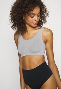 Sujetador seamless gris claro con tirantes anchos y escote curvado, combinado con braguitas negras de cintura alta. Se puede apreciar la suave textura de la tela.