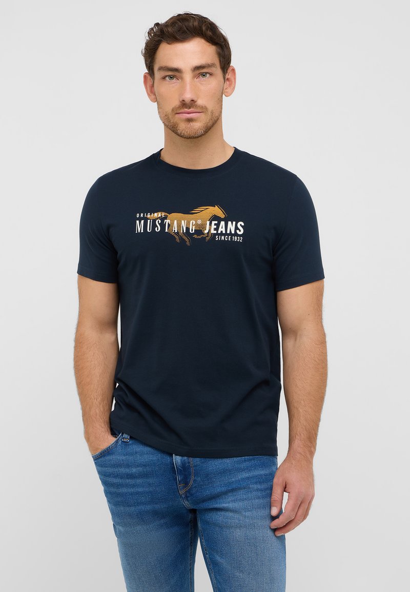 Tamsiai mėlyna trump sleeves marškinėliai, pasiūti iš medvilnės, su priekyje esančiu grafinio dizaino su arklių motyvu ir tekstu "Mustang Jeans nuo 1932 metų."