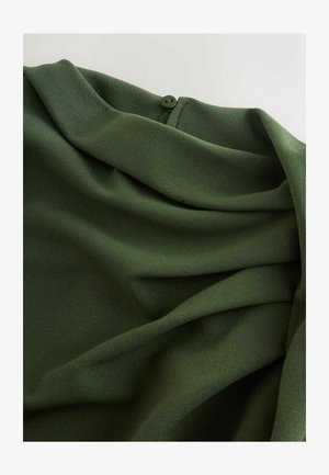Dark green textured fabric with folds and a small round green button near the top edge on a light background.