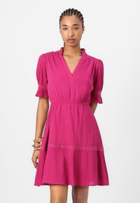 Roze jurk met pofmouwen, v-hals en decoratieve taille. Beschikt over een tekstuurstof en een uitlopende rok met een geschulpte zoom.