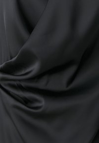 Svart stoff med en glatt, satenglignende tekstur, med myke folder og draperinger, som reflekterer lys subtilt over overflaten.