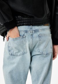Jeans de mezclilla azul claro con un corte relajado, que cuentan con dos bolsillos traseros, textura desgastada y una cinturilla alta. Combinados con una chaqueta de cuero negra.