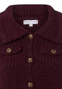 Burgunderfarbene Wolljacke mit strukturiertem Strickdesign, ausgestattet mit einem Kragen, zwei Brusttaschen und goldfarbenen Knotenknebeln. Auffälliges Markenetikett sichtbar.