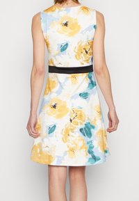 Vestido floral con patrones amarillos y azules, diseño sin mangas, cinturón negro en la cintura, tela suave y falda acampanada. Vista trasera mostrada.