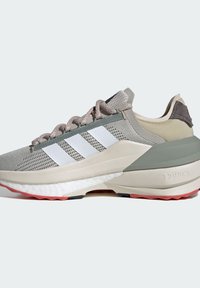 Zapatilla deportiva en tonos gris y beige con parte superior de malla, diseño de tres rayas blancas y suela texturizada con acentos en rosa y negro.