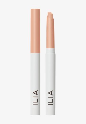 Deux sticks de correcteur de la marque ILIA avec des capuchons couleur pêche, l’un fermé et l’autre ouvert montrant le produit crème biseauté, debout sur fond blanc.