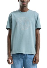 T-shirt turquoise à manches courtes en coton doux, avec un logo circulaire délavé imprimé à l'avant, doté d'une coupe décontractée.