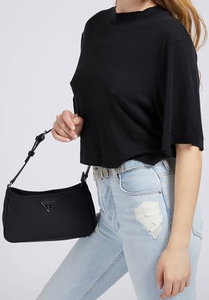 Bolso negro con un logo triangular, diseño elegante y una correa corta. Combinado con una camiseta negra corta y jeans desgastados de color azul claro.