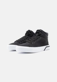 Černé vysoké tenisky vyrobené z plátna s černými tkaničkami, bílou gumovou podrážkou a minimalistickými akcenty, s texturovaným povrchem.