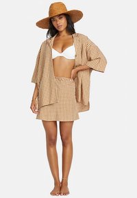 Brown and white gingham print outfit featuring a loose-fitting button-up shirt and matching skirt, complemented by a wide-brim straw hat.