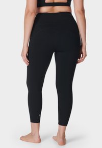 Zwarte high-waisted leggings van rekbaar materiaal, met een zachte textuur en subtiele stikdetails, die net onder de kuit eindigen.