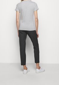 Grå bomulds t-shirt med opsmøgede ærmer, parret med skræddersyede sorte bukser og hvide sneakers, set fra ryggen.