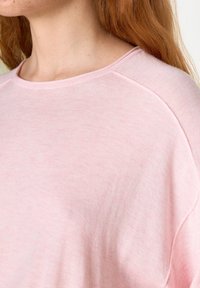 Svetle růžová mikina s žebrovaným kulatým výstřihem a raglánovými rukávy. Látka vypadá měkce s mírně texturovaným povrchem.