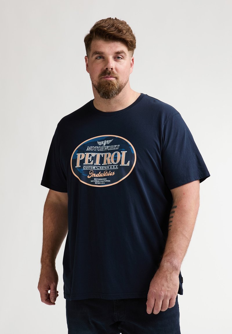 T-shirt en coton bleu marine avec un motif circulaire de style vintage arborant le texte "PETROL" en blanc et bleu sur le devant, manches courtes et col rond.